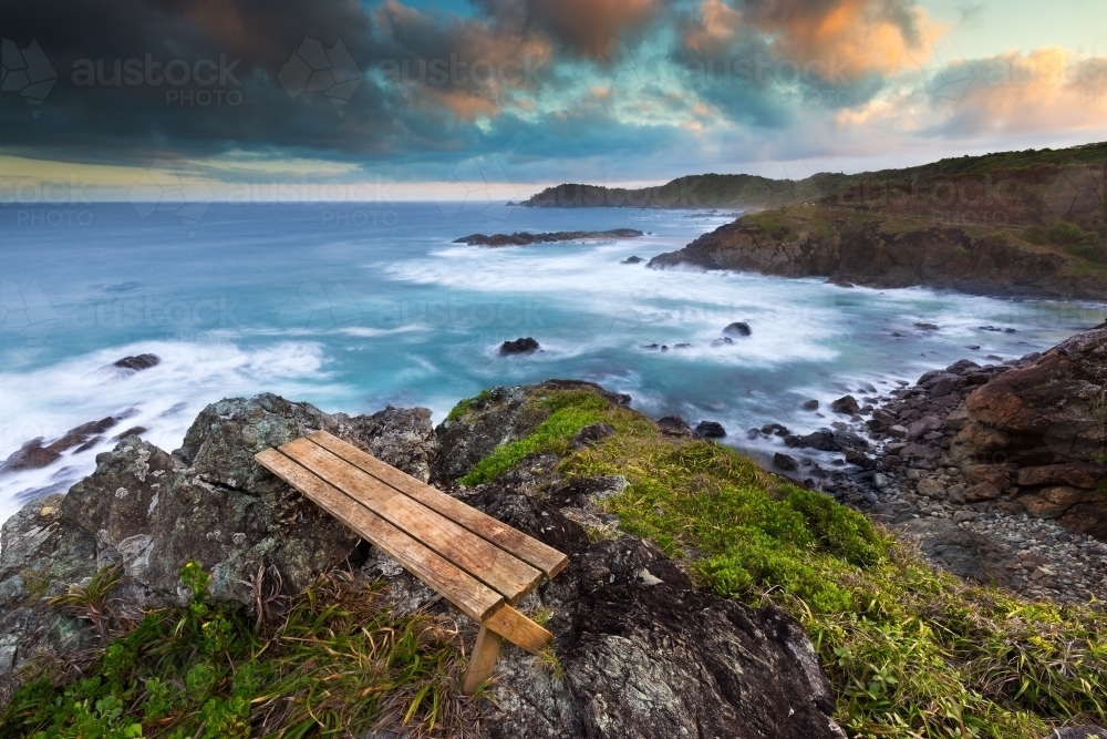Coastline view from headland with a wooden bench on a stormy day - Australian Stock Image