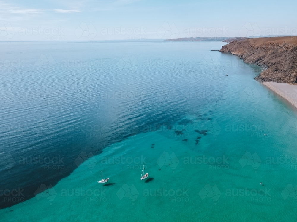 Coastline with rolling hills and boats and two tones coloured blue ocean from above - Australian Stock Image