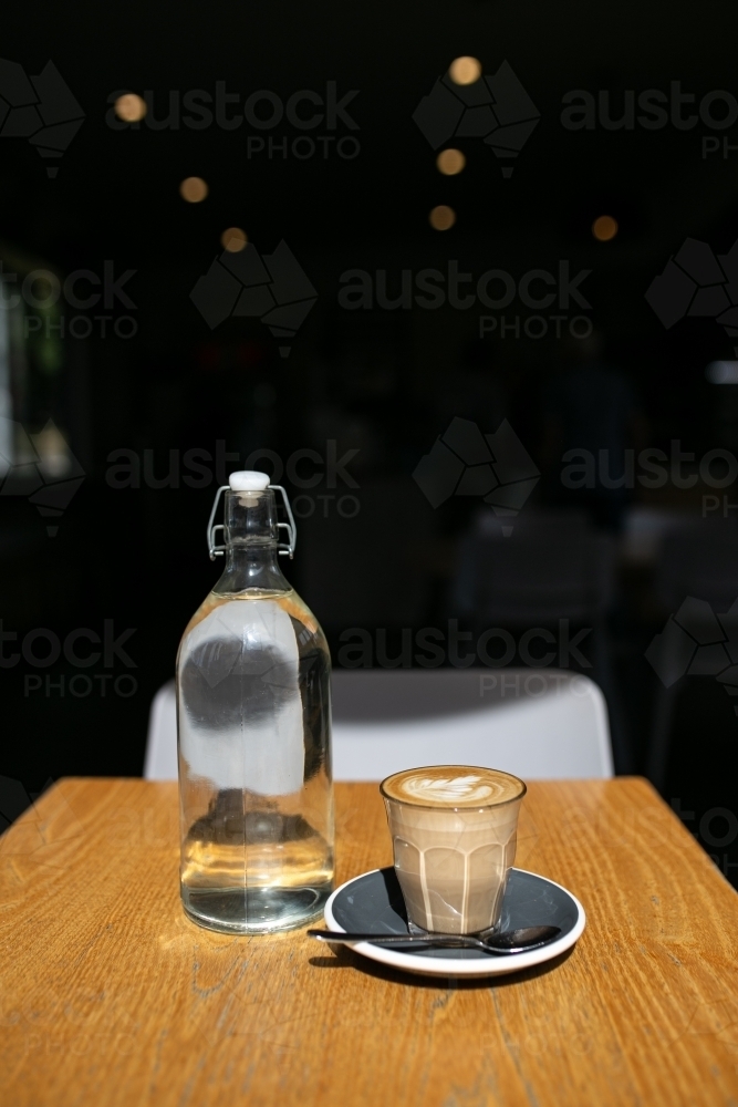 Coffee art in glass cup on a table with a teaspoon and a bottle of water - Australian Stock Image
