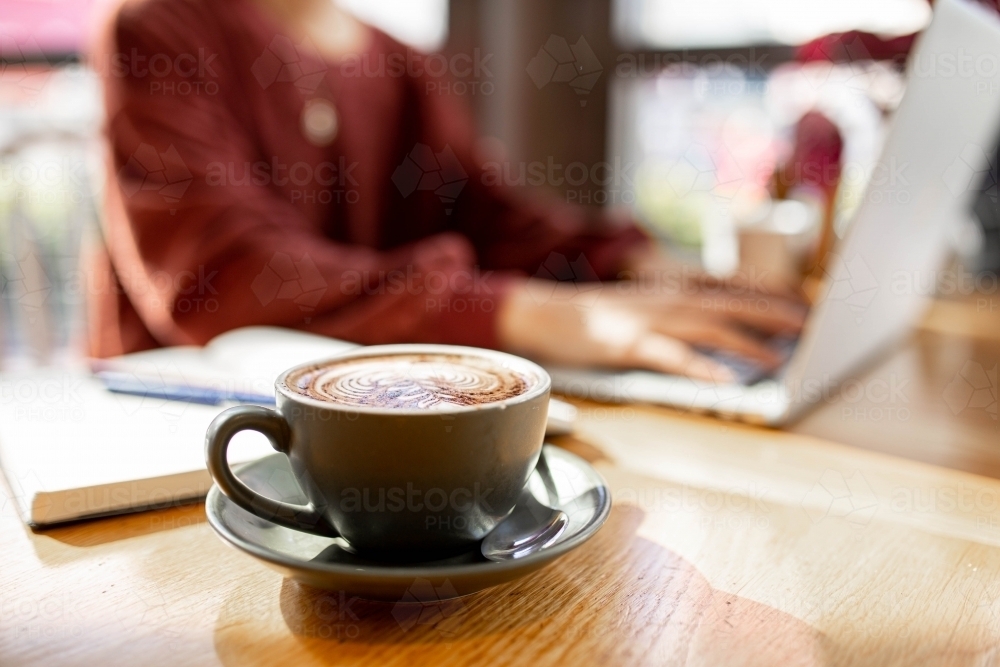 coffee on table of person working remotely on her laptop at a cafe - Australian Stock Image