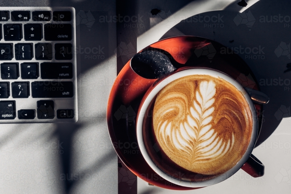 Coffee with latte art sat next to an opened laptop - Australian Stock Image