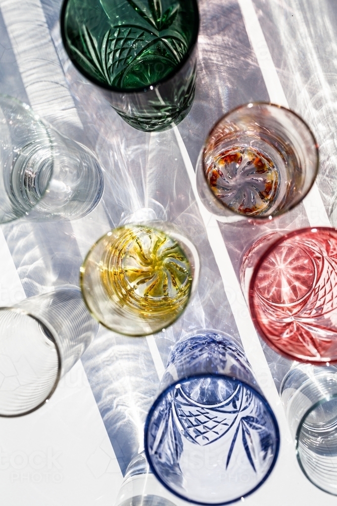 Collection of glasses on table top casting textured shadows with split light - Australian Stock Image