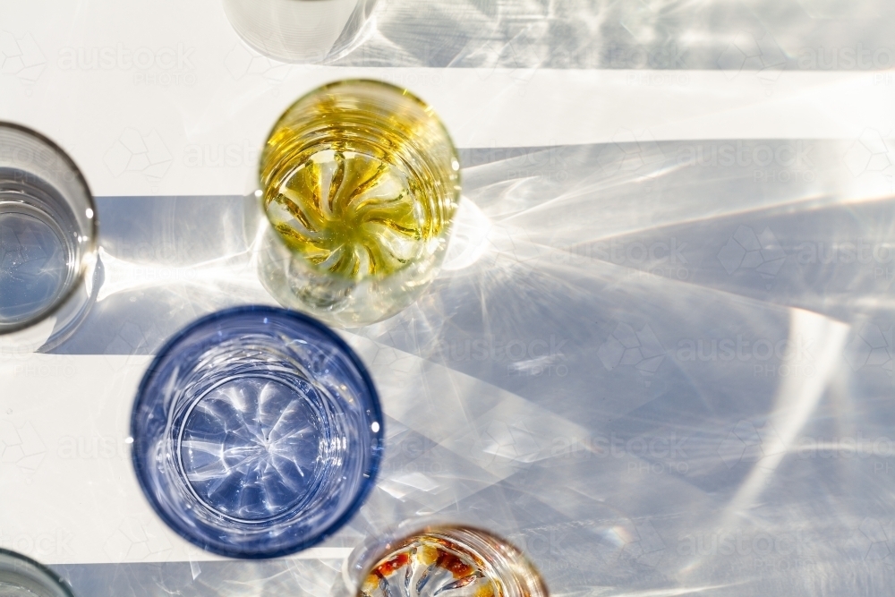 Collection of glasses on table top casting textured shadows with split light - Australian Stock Image