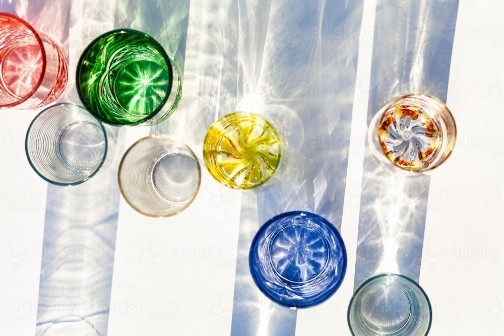 Collection of glasses on table top casting textured shadows with split light - Australian Stock Image