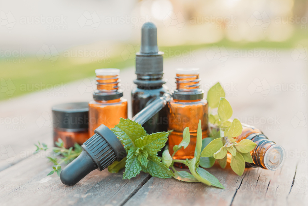 Collection of various amber essential oil bottles in natural outdoor setting with fresh herbs - Australian Stock Image