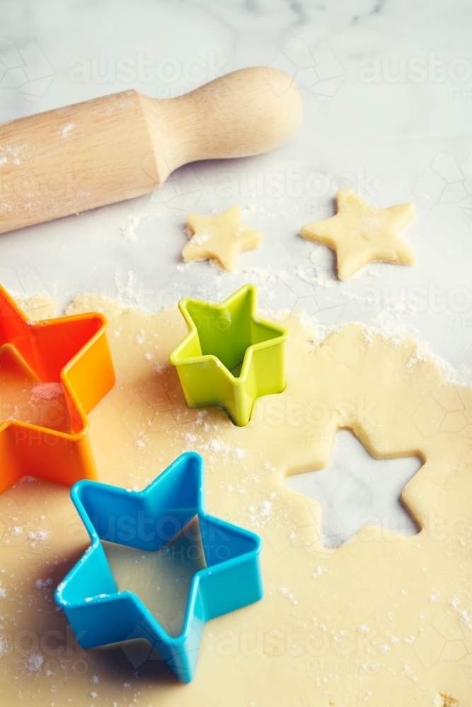 Colored star shaped cookie cutters in dough vertical - Australian Stock Image