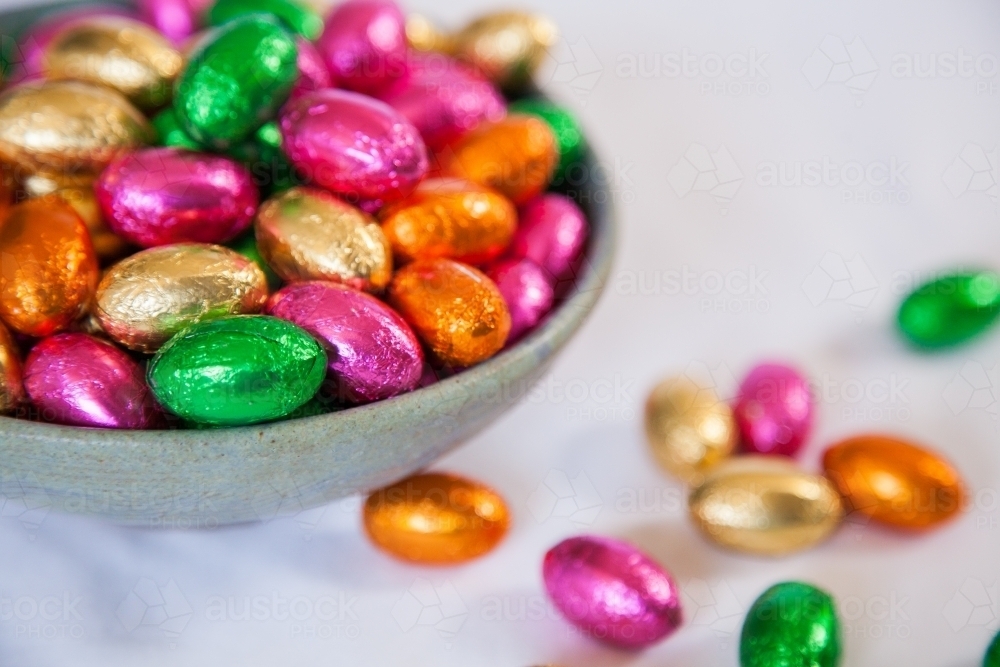 Colorful, foil wrapped Easter eggs in a bowl on white - Australian Stock Image