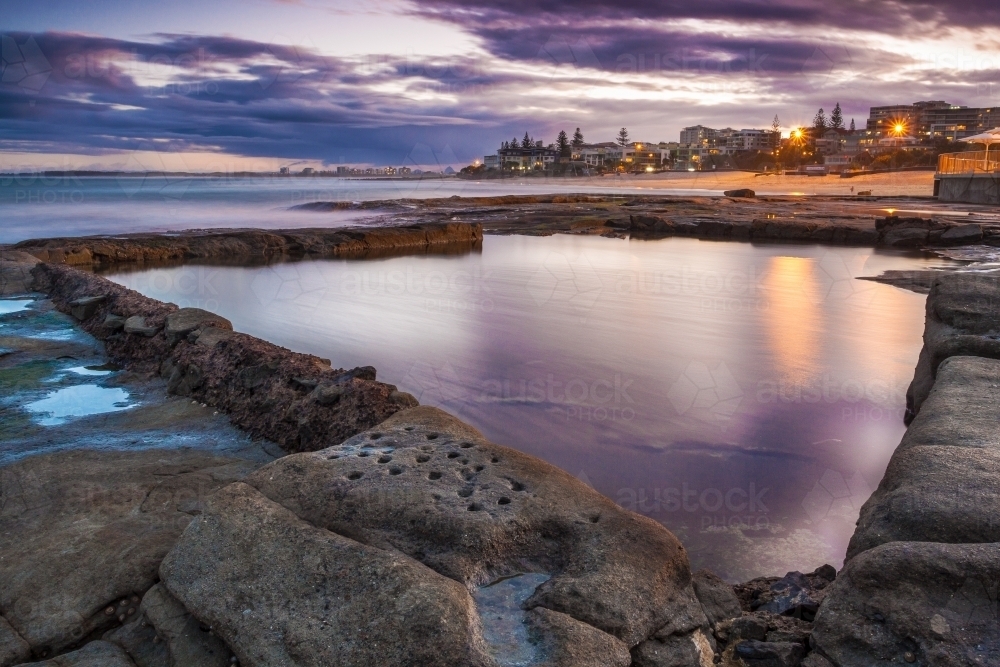Colorful reflection in a large rock pool along a city beach at twilight - Australian Stock Image