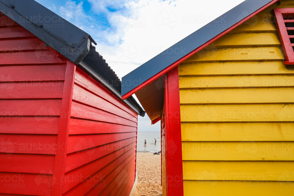 Colourful beach huts in red and yellow under a partly cloudy sky by the ocean - Australian Stock Image