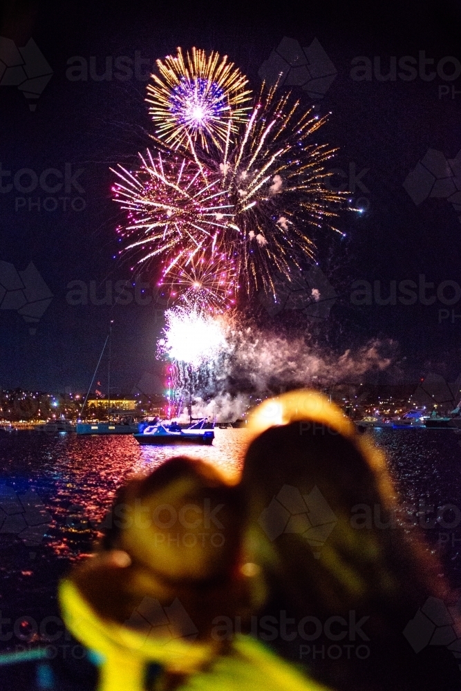 Colourful fireworks display over water with out of focus people in foreground - Australian Stock Image