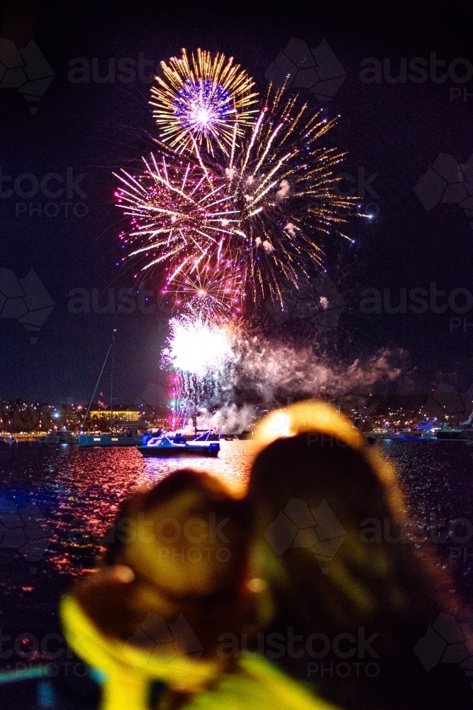Colourful fireworks display over water with out of focus people in foreground - Australian Stock Image
