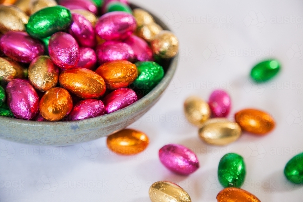 Colourful, foil wrapped Easter eggs in a bowl on white - Australian Stock Image