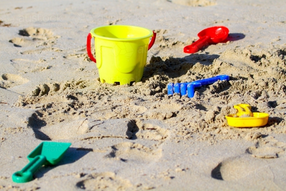 Colourful plastic bucket, rake, shovel and other toys on a sandy beach. - Australian Stock Image