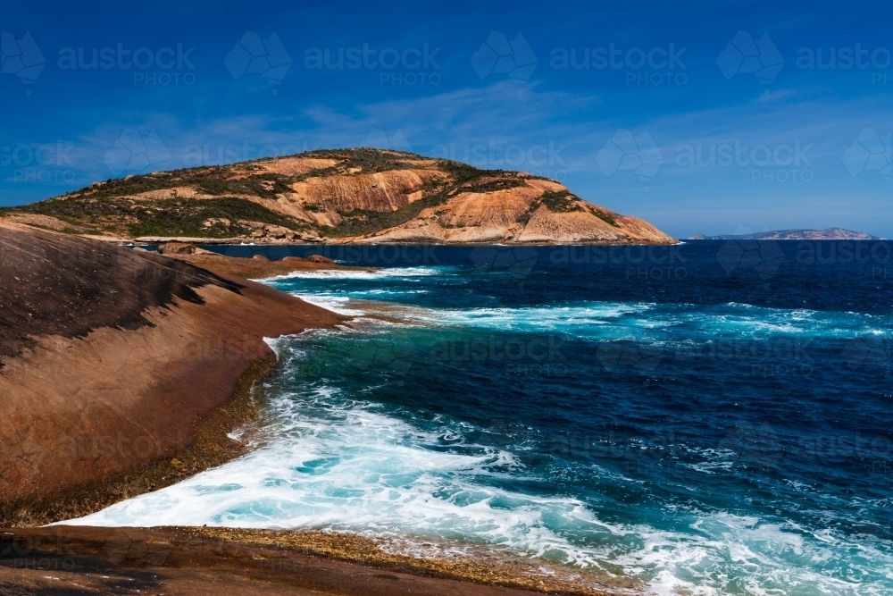 Colourful rocky foreground with dark turquoise water and deep blue sky - Australian Stock Image