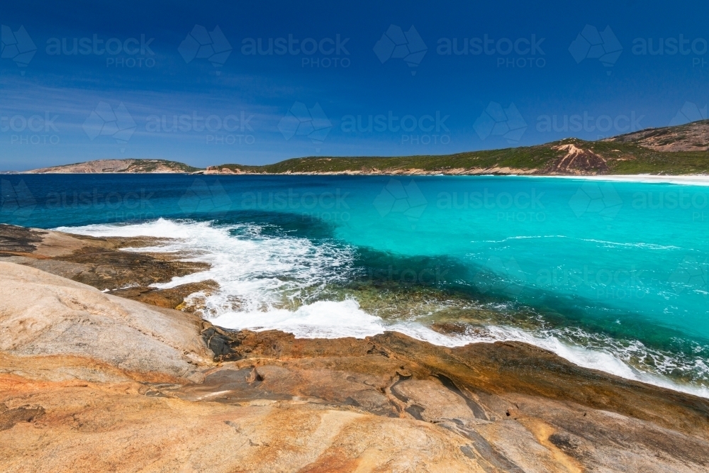 Colourful rocky foreground with waves and turquoise water and sweeping view of coastline - Australian Stock Image