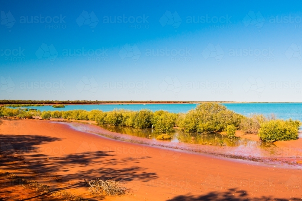 Colourful seascape, with layers of red sands, green mangroves, turquoise water and clear blue sky - Australian Stock Image