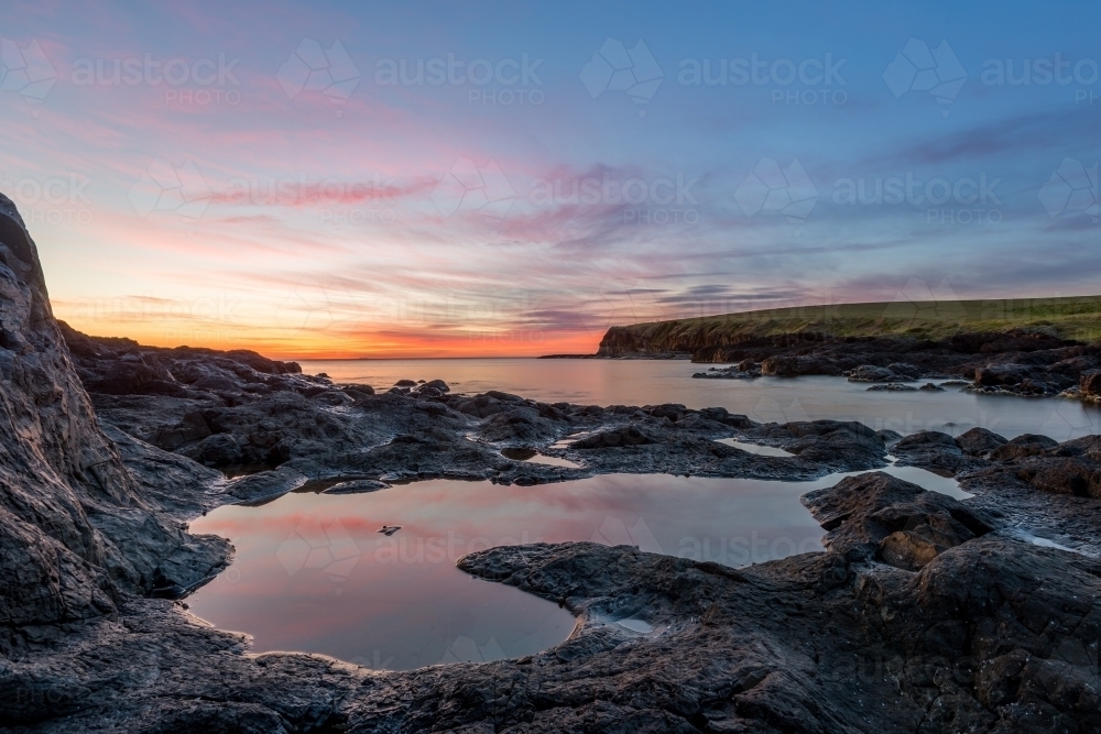 Colourful sunrise reflecting in ocean rock pools - Australian Stock Image