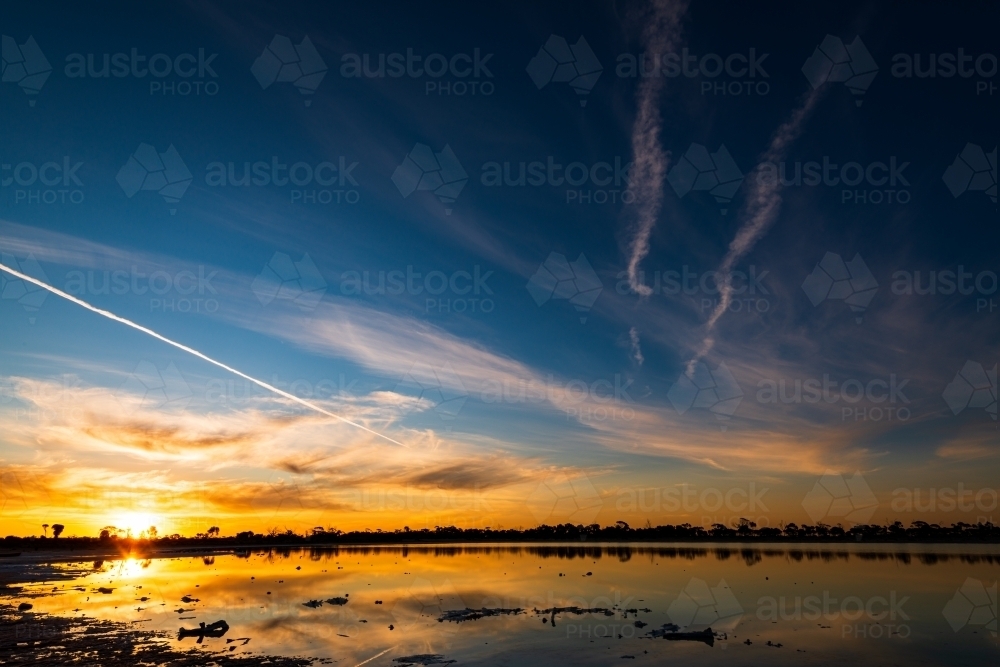 Colourful sunset over a lake with jet streams and reflections - Australian Stock Image