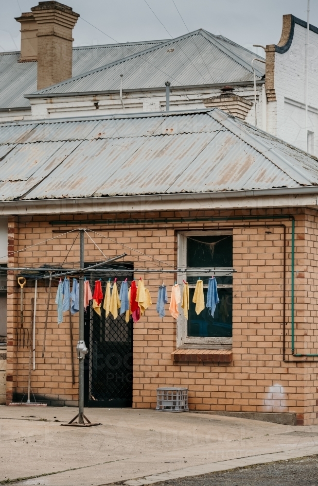 Colourful towels hung on hills hoist washing line outside a brick house - Australian Stock Image