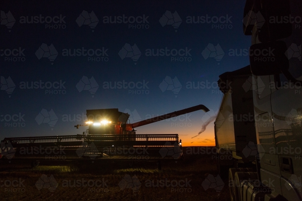 Combine harvester about to unload grain into a semi trailer truck at night - Australian Stock Image