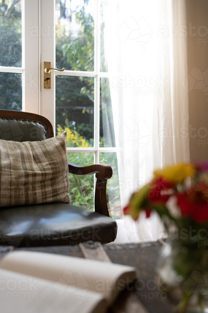 Comfortable chair by window with book and flowers - Australian Stock Image