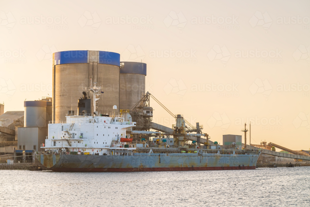 Commercial cement carrier at Port Adelaide docks viewed across the Port River at sunset - Australian Stock Image