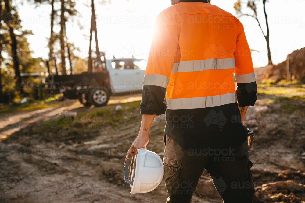 Construction worker holding a helmet and a drill while walking on the construction site. - Australian Stock Image