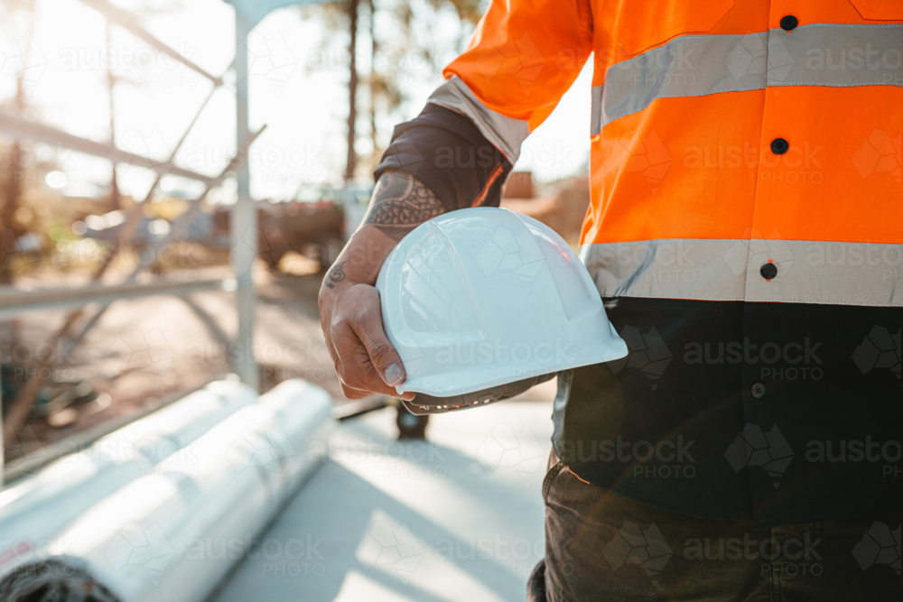 Construction worker holding a white helmet at construction site. - Australian Stock Image