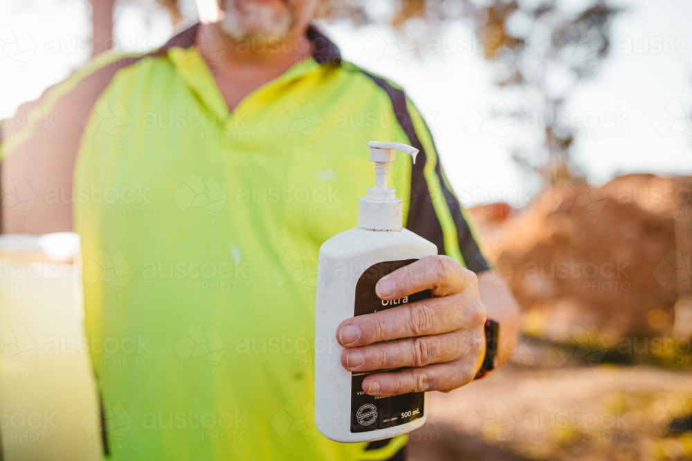 Construction worker on a blurry background holding sunscreen pump bottle - Australian Stock Image