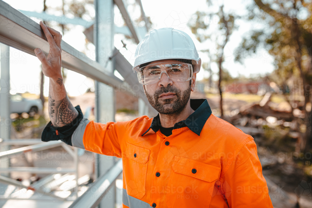 Construction worker standing beside the metal structure in the construction site. - Australian Stock Image