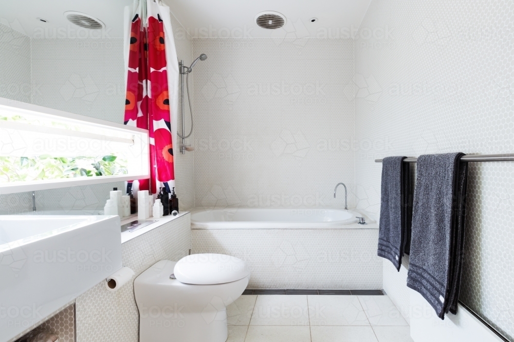 Contemporary white bathroom of mosaic and terrazzo tiles with red shower curtain - Australian Stock Image