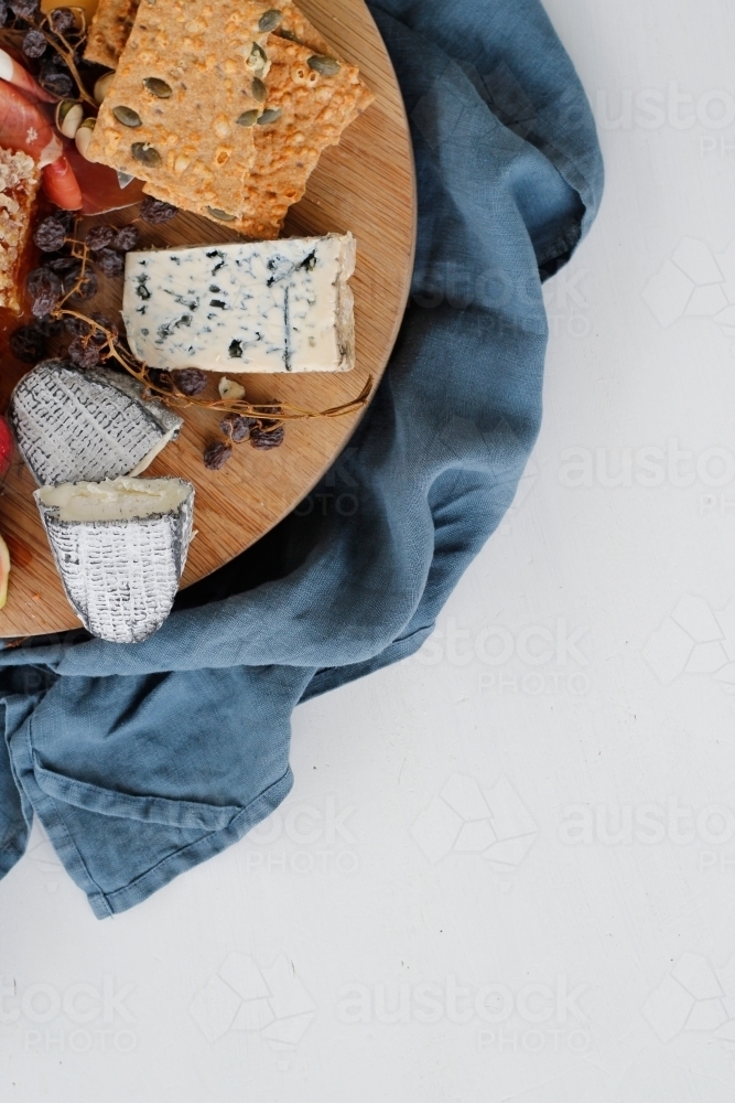 Corner of cheese platter with cheese, crackers and dried fruit on blue linen cloth - Australian Stock Image