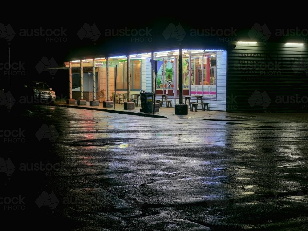 Image of Corner store at night with light reflected on a wet road Austockphoto