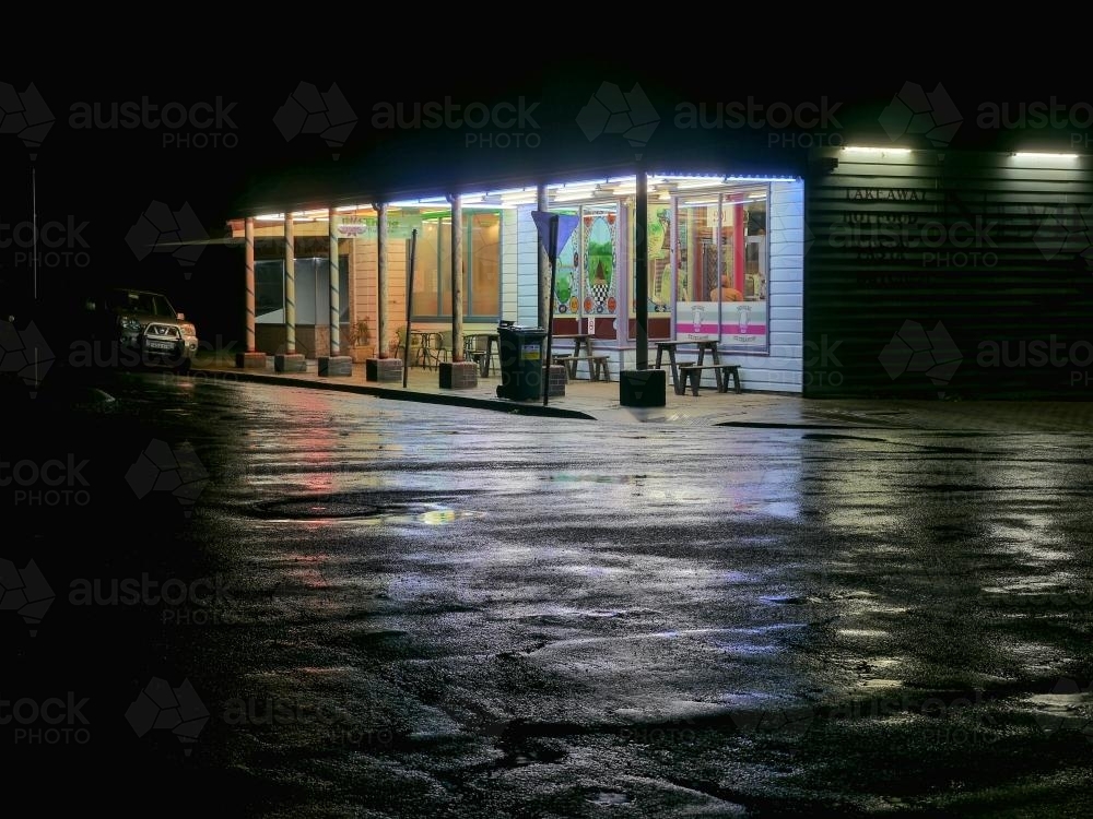 Corner store at night with light reflected on a wet road - Australian Stock Image