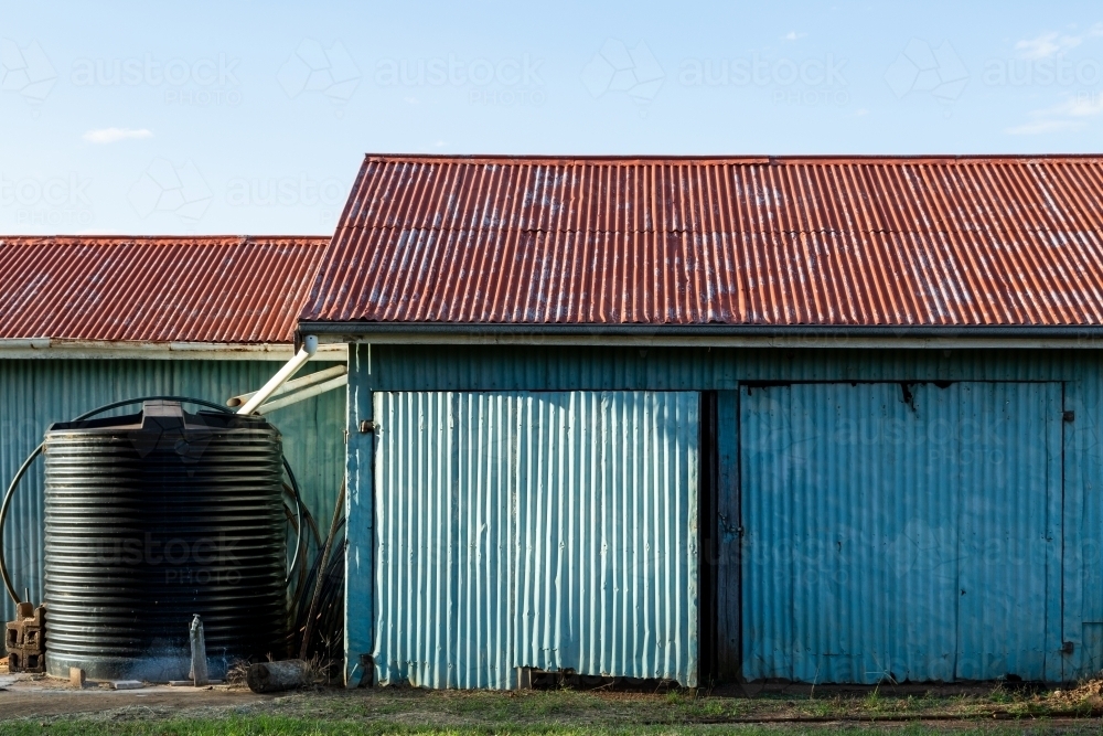Corrugated iron farm shed painted blue, with red roof, and water tank. - Australian Stock Image