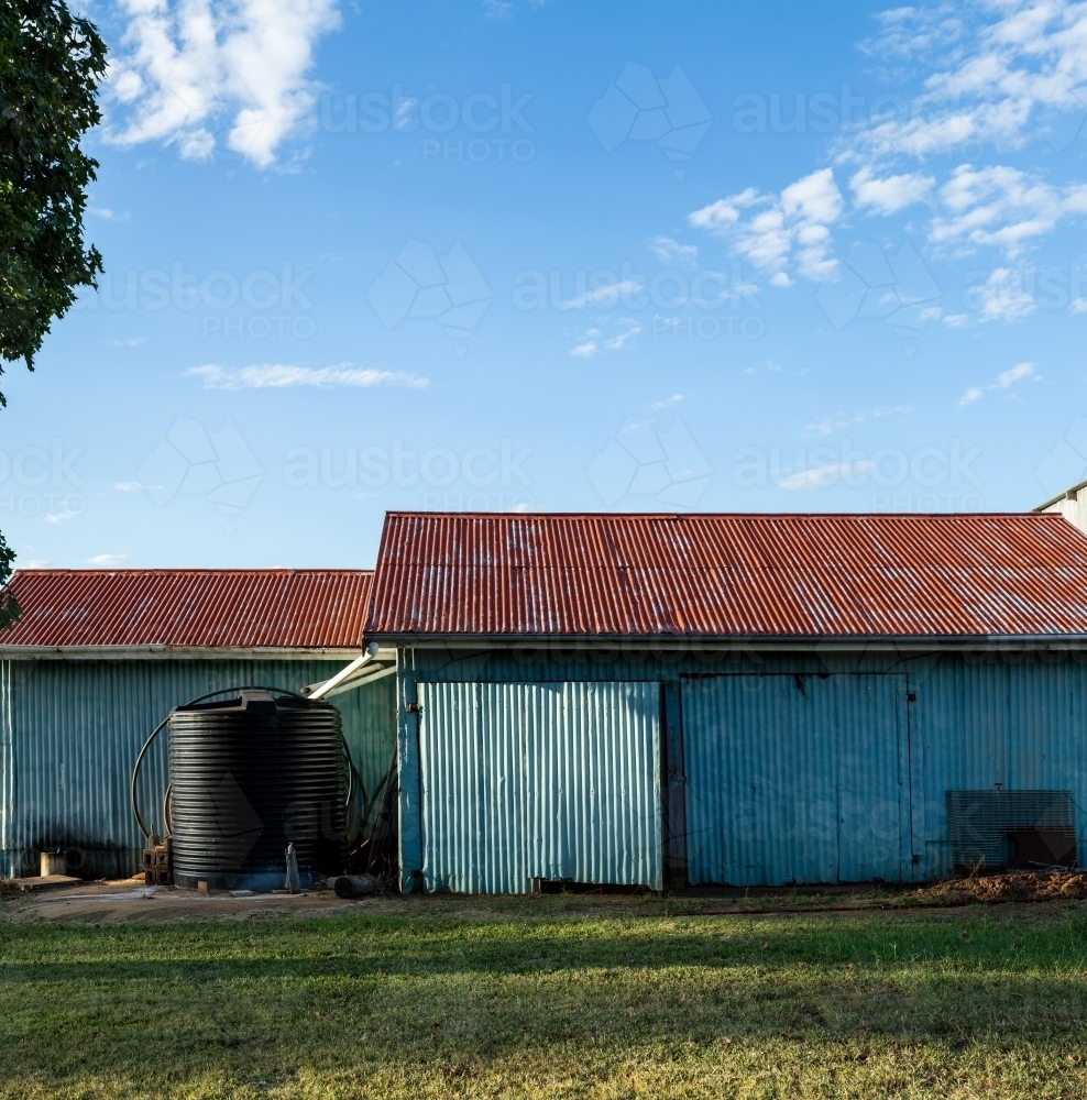 Corrugated iron farm shed painted blue, with red roof, and water tank. - Australian Stock Image