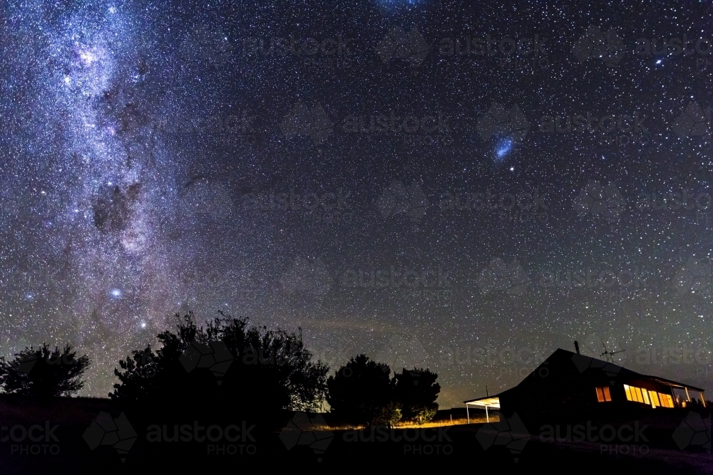 Cottage at night with lights in windows and starry sky - Australian Stock Image
