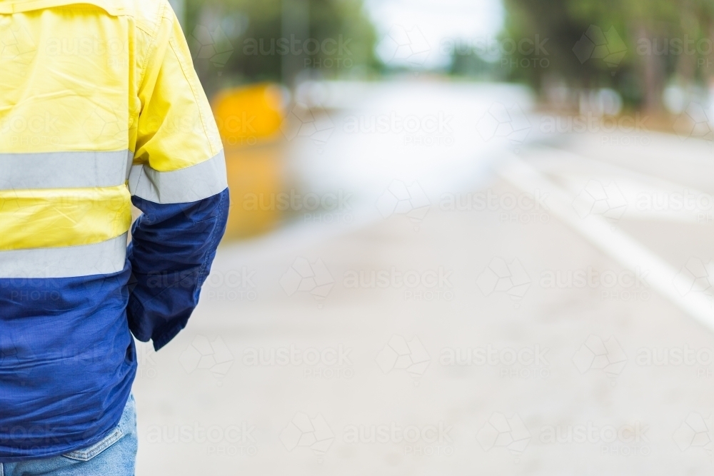 Council worker in high vis with copy space and floodwater over road - Australian Stock Image