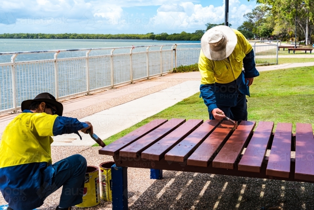 Council workers painting outdoor park benches and tables in Moreton Shire - Australian Stock Image