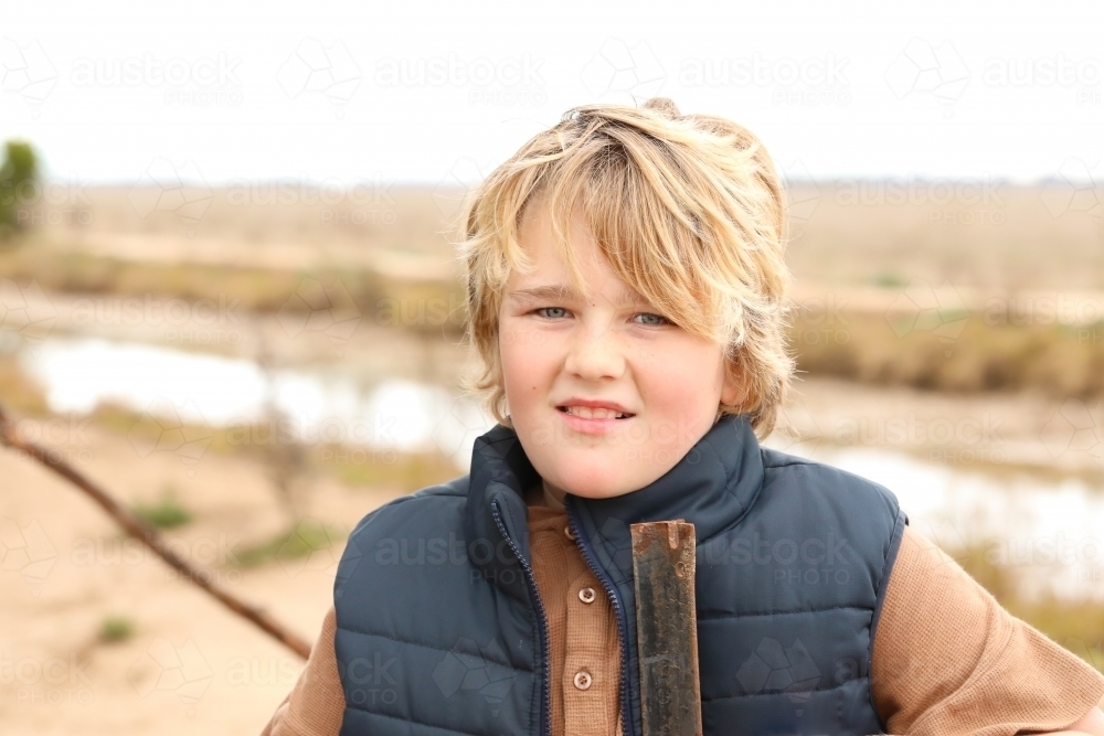 Country boy leaning on farm fence with dry paddock in background - Australian Stock Image