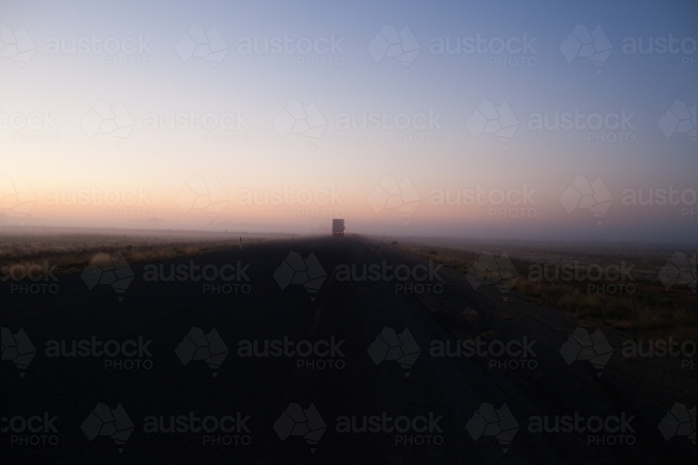 Country highway at sunrise with semi trailer truck driving off in distance - Australian Stock Image