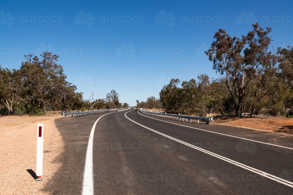 Country highway with white line markings and cats eye post and converging lines. - Australian Stock Image