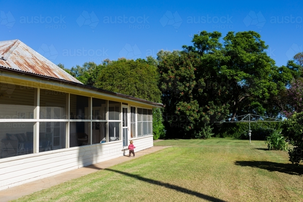 Country kid toddler walking on path around farm house homestead on sunlit day in Australia - Australian Stock Image