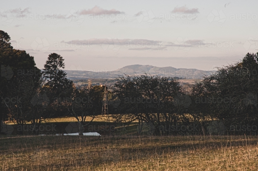 country pasture view at sunset with a windmill and mountains in th background - Australian Stock Image