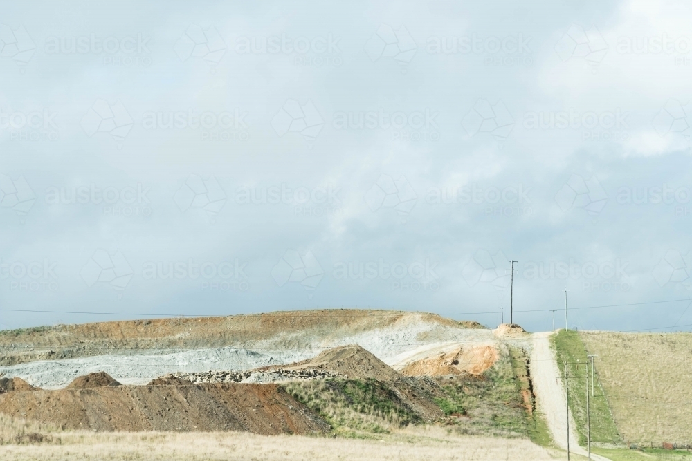 country road leading over a hill past an old quarry in muted tones - Australian Stock Image