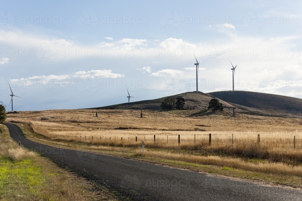 Country road leading through paddocks with wind turbines - Australian Stock Image