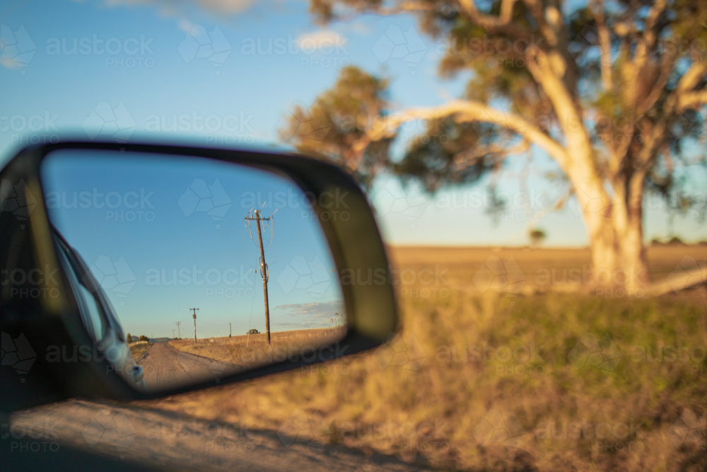 Country road lined with power lines visible in side mirror of car on rural Australian road trip - Australian Stock Image