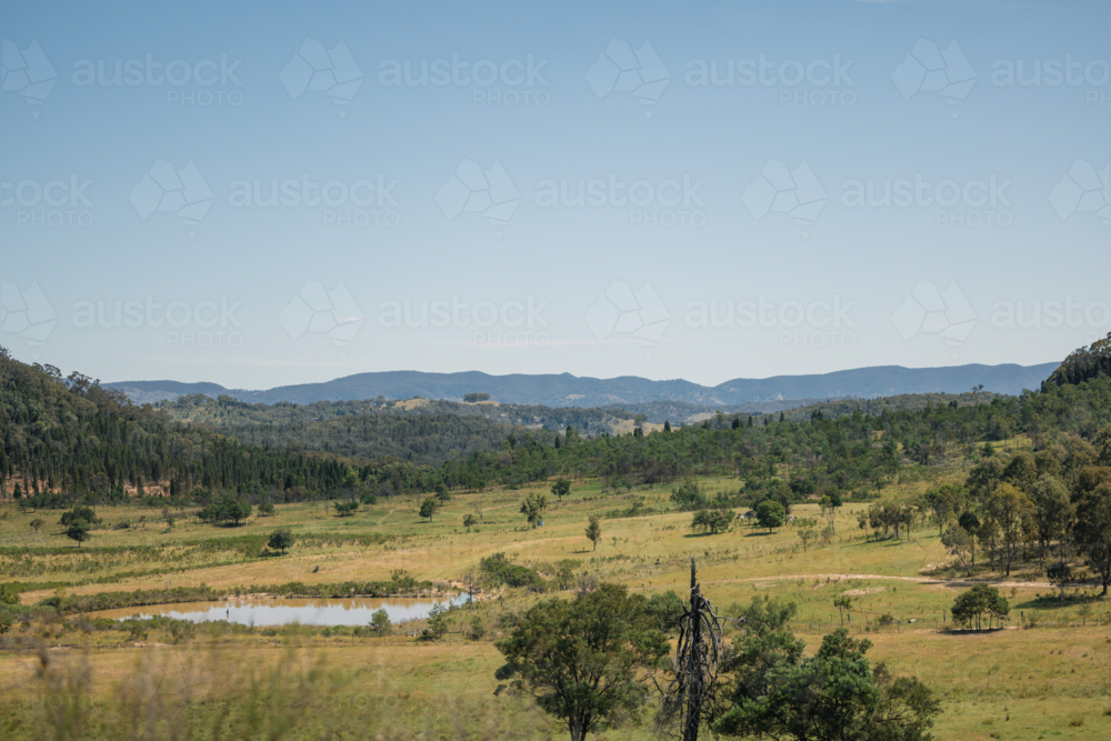 Countryside landscape with rolling hills and green pastures under a clear blue sky - Australian Stock Image