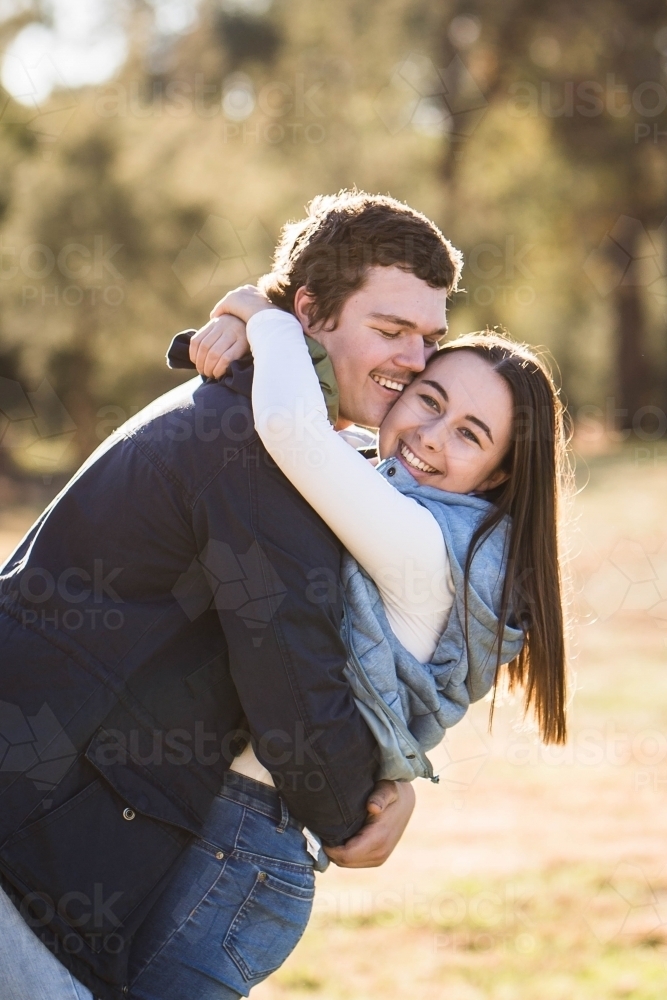 Couple cuddling arms wrapped tight smiling - Australian Stock Image
