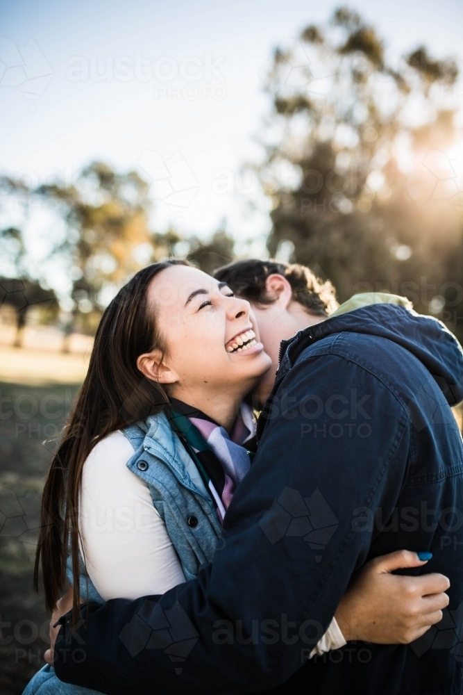 Couple cuddling woman laughing while man kisses her neck - Australian Stock Image